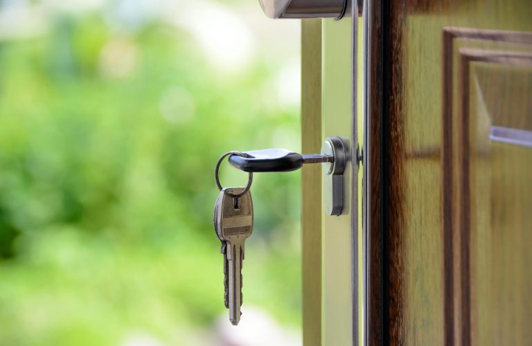 Key inserted in door lock against a blurred green background, symbolizing security and real estate.